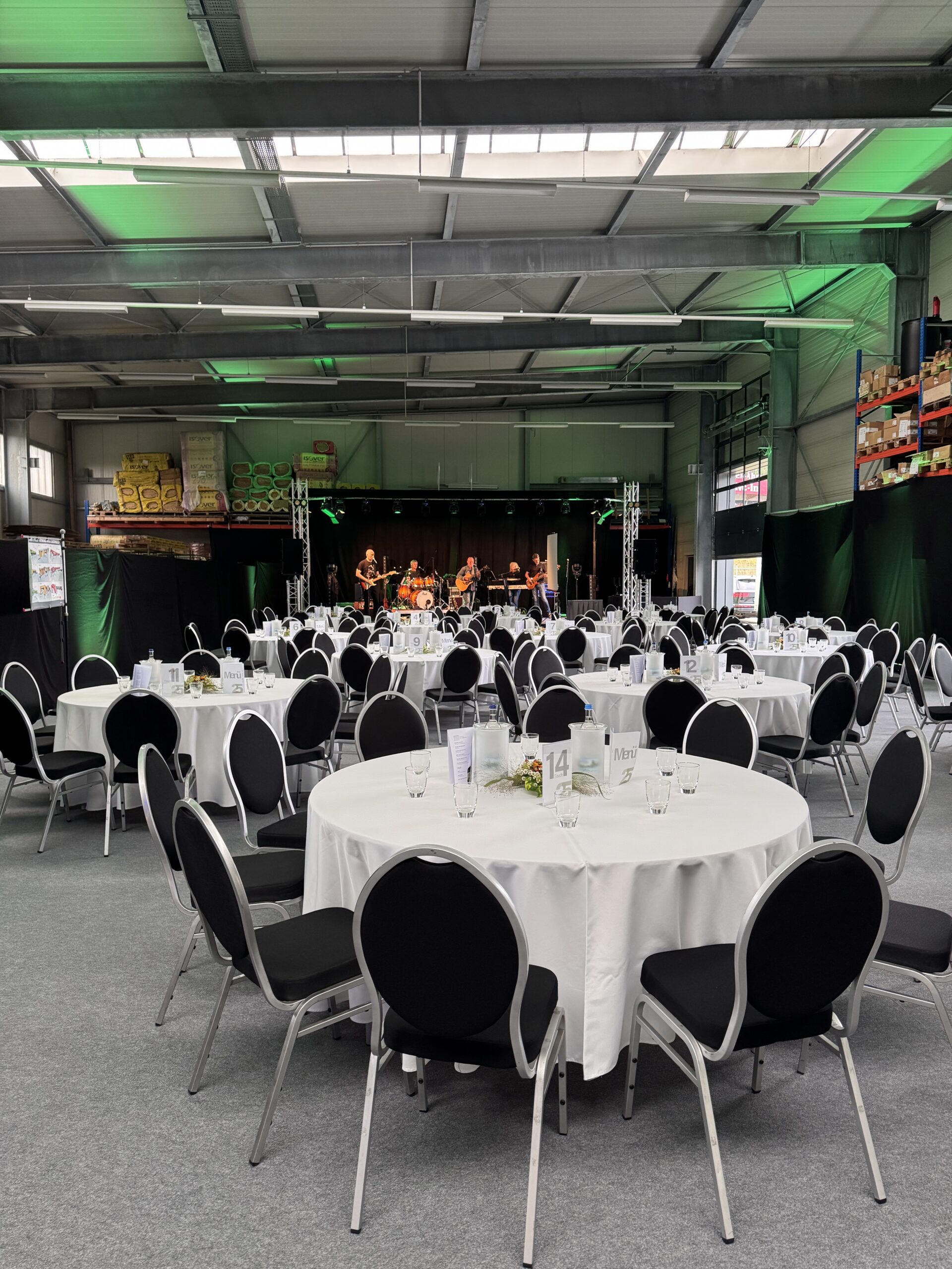 Firmenjubiläum in einer Halle mit Gästen, runden Tafeln und Bühne