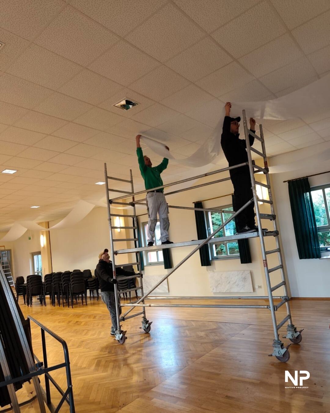 Unser Team hängt auf Gerüsten Deckenstoffe im Saal auf